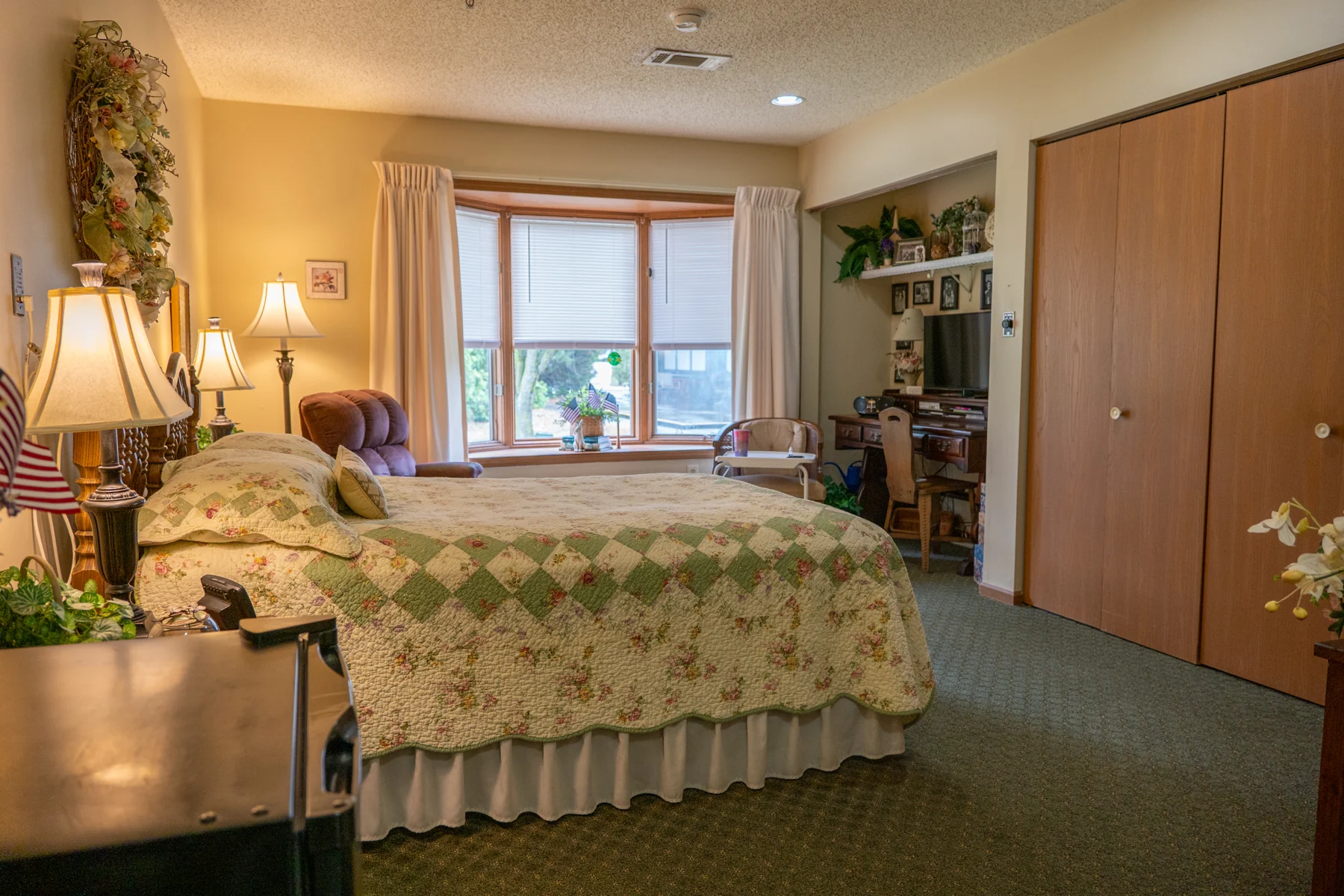 A residential bedroom with a quilt and sunlit bay window
